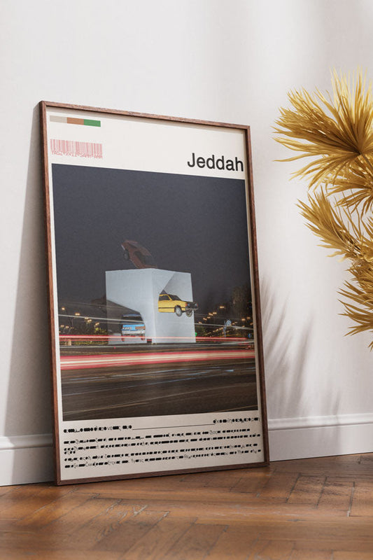 Framed poster of Jeddah on a wall next to a wooden chair and decorative plants.