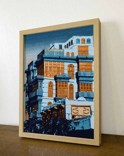 Framed artwork of a building on a wooden surface with a white wall background