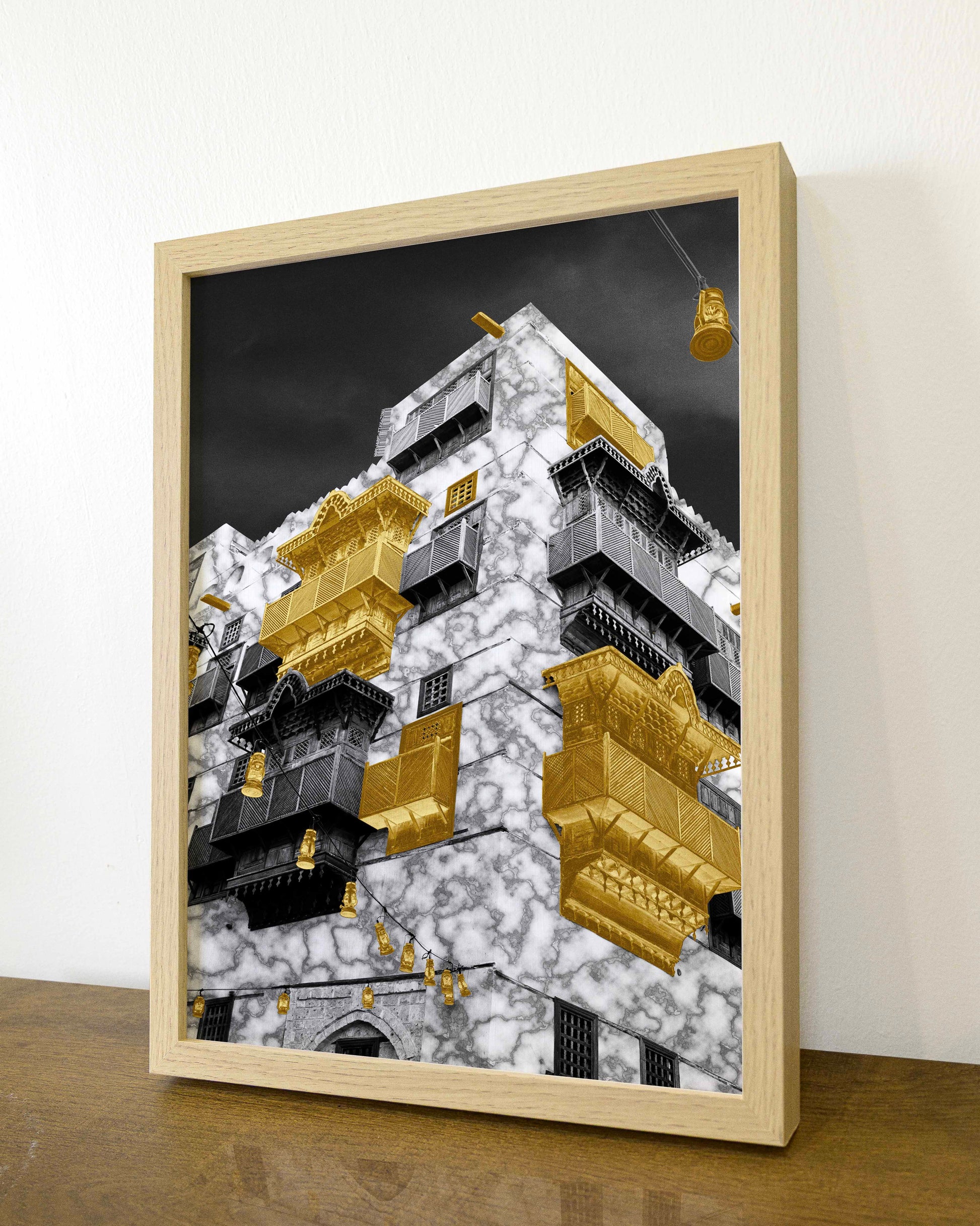Framed artwork of a modern building with gold accents on a wooden surface.