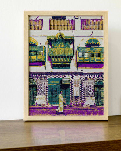 Framed artwork of a colorful street scene with buildings and a person walking.
