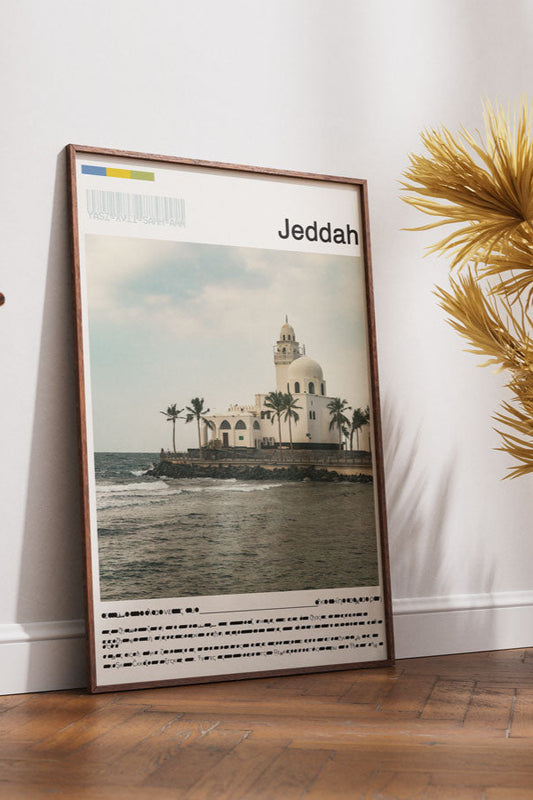 Framed poster of Jeddah on a wall next to a wooden chair and decorative plants.